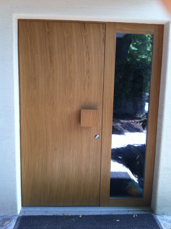 Schöne, grosse Holztüre mit Fensteraussparung neben der Türe. Die Firma Weidmann AG in Möhlin hat die passenden Türen für Ihr Zuhause.