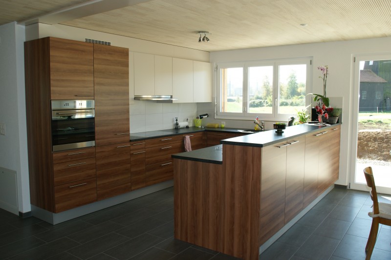 Holzküche in schönem, modernen Design mit ergänzenden, weissen Hängeschränken und schwarzer Arbeitsfläche aus Kunststoff. Die Firma Weidmann AG in Möhlin baut Ihre Küche nach Ihren Wünschen.