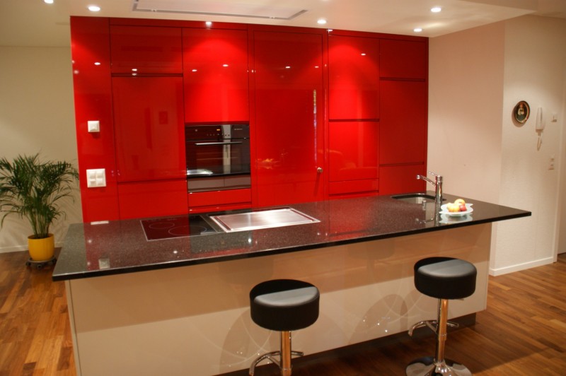 Rote, massive Glanzküche und schöner Kücheninsel in weiss mit schwarzer Steinabdeckung. Die Firma Weidmann AG in Möhlin baut Ihre Traumküche.