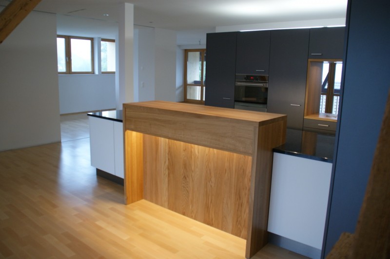 Moderne Küche mit blauer Verkleidung, Holzbar und schwarzer Marmor Ablagefläche. Küchenbauten von der Firma Weidmann AG in Möhlin.