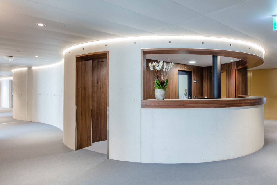 Die Rezeption des Merian Iselin Krankenhauses in Basel mit schönen dunklen Holzschränken im Hintergrund und eine passende Holzverkleidung des Empfangs. Schöner Innenausbau von der Firma Weidmann AG in Möhlin.